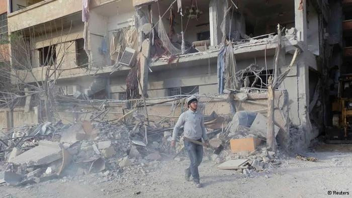 A man carrying a shovel, walks near buildings damaged after what activists said was a Syrian Air Force fighter jet operated by those loyal to Syria