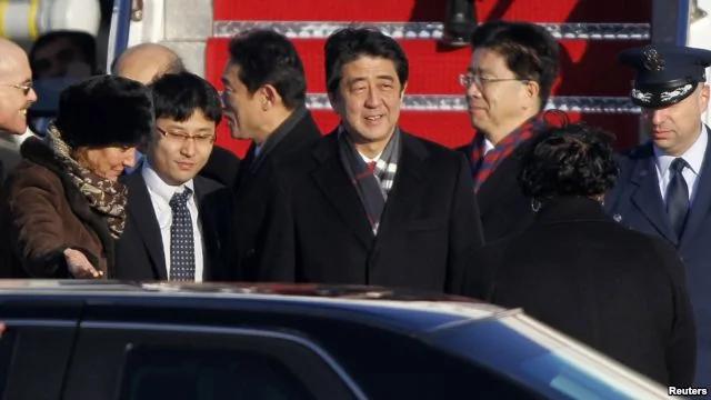 2013年2月21日，日本首相安倍晋三(中)抵达华盛顿附近安德鲁斯空军基地，美国首席礼宾官卡普丽奇娅?马歇尔(左)到机场迎接。
