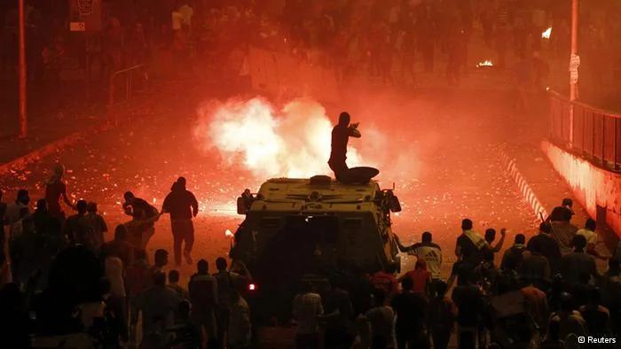 A riot police officer, on a armoured personnel carrier surrounded by anti-Mursi protesters(foreground), fires rubber bullets at members of the Muslim Brotherhood and supporters of ousted Egyptian President Mohamed Mursi along a road at Ramsis square, which leads to Tahrir Square, during clashes at a celebration marking Egypt