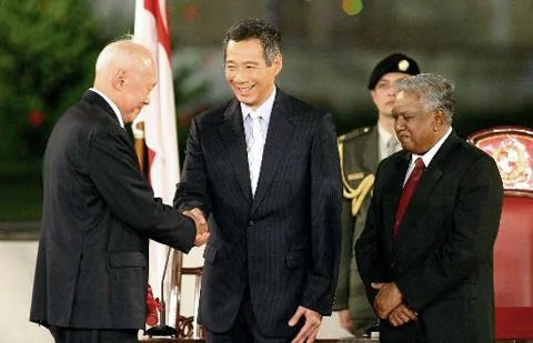 图为李显龙于2004年8月12日就任新加坡总理时与父亲 - 新加坡资政李光耀握手。右为新加坡总统纳珊