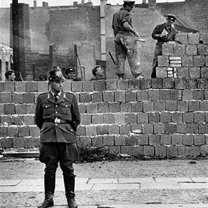 圖為1961年10月7日一名西柏林士兵站立在分割東、西柏林的混凝土牆邊。他身後為東柏林工人正在加高圍牆
