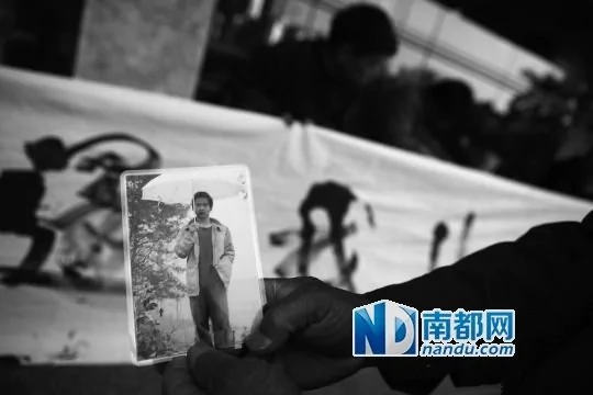 在李茂韬工作的公司门前，李父展示儿子生前的照片。南都记者霍健斌实习生刘羽洁摄