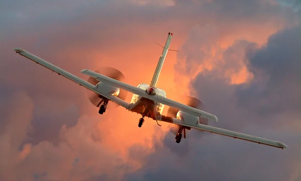 A plane flies into a sunset