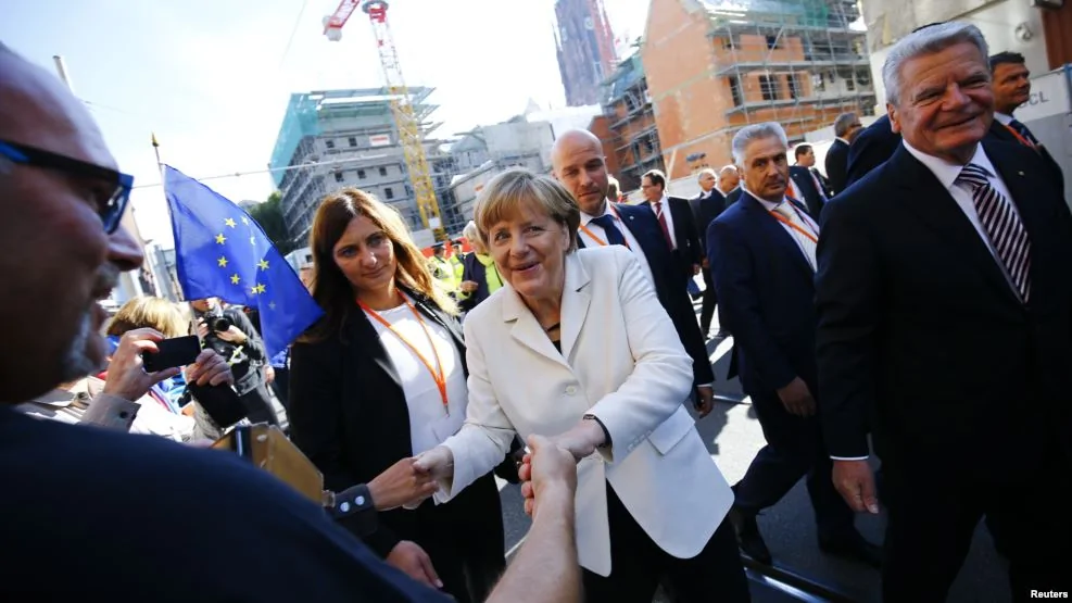 德国总理高克(右），总理默克尔（中）和街上行人（2015年10月3日）