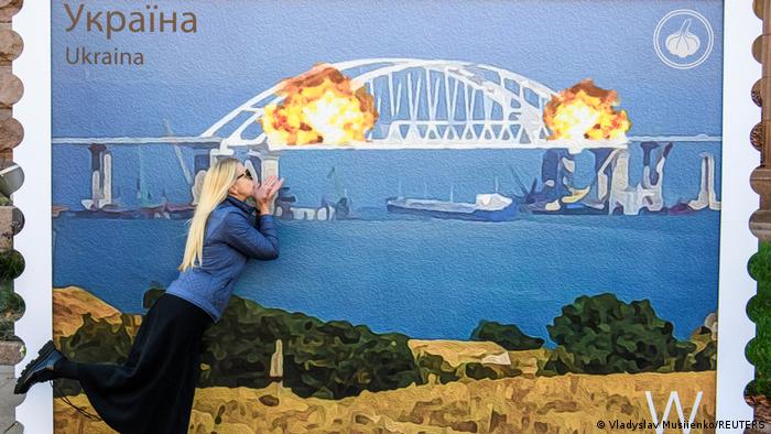 在基辅，一名乌克兰女子在展示刻赤大桥爆炸的画报前留影