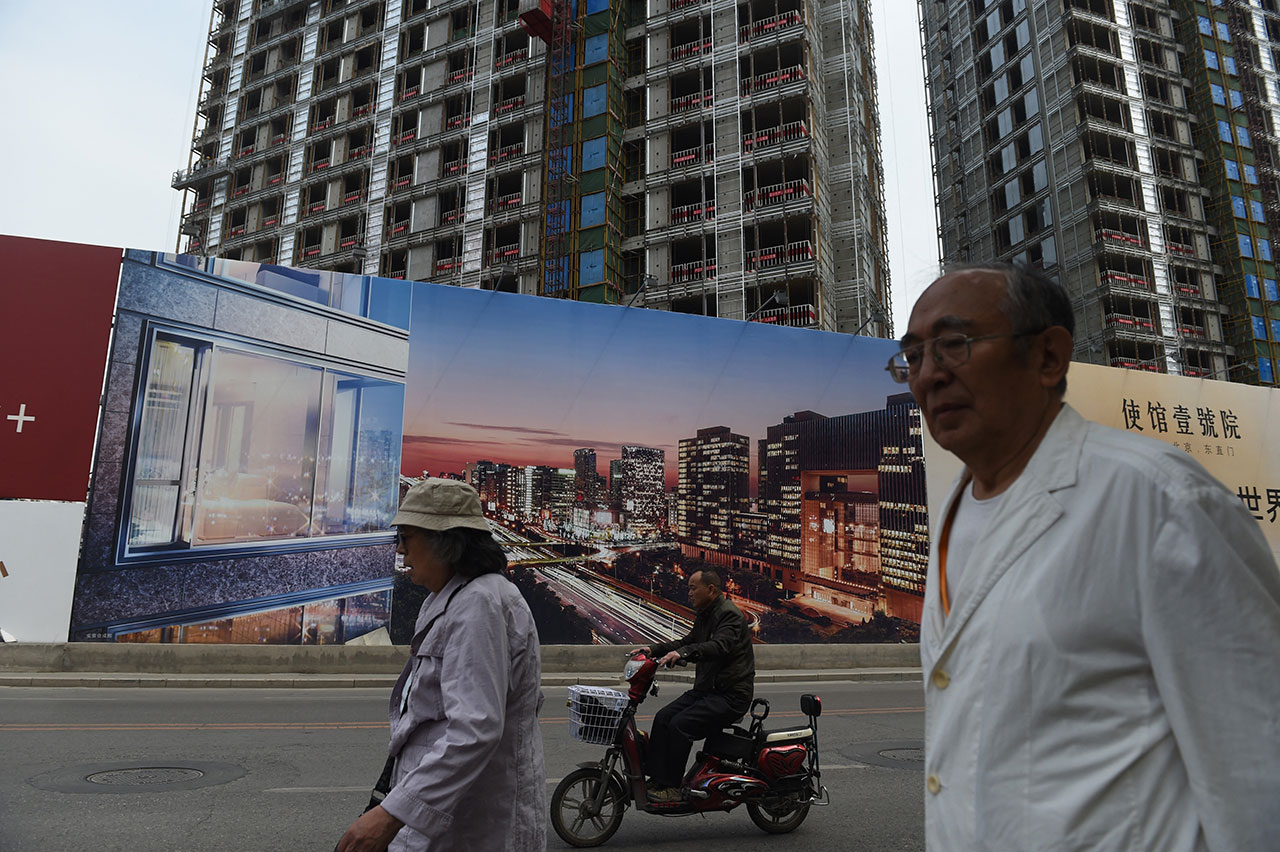 北京市民走过一处建筑工地外的新住宅区广告牌（法新社）