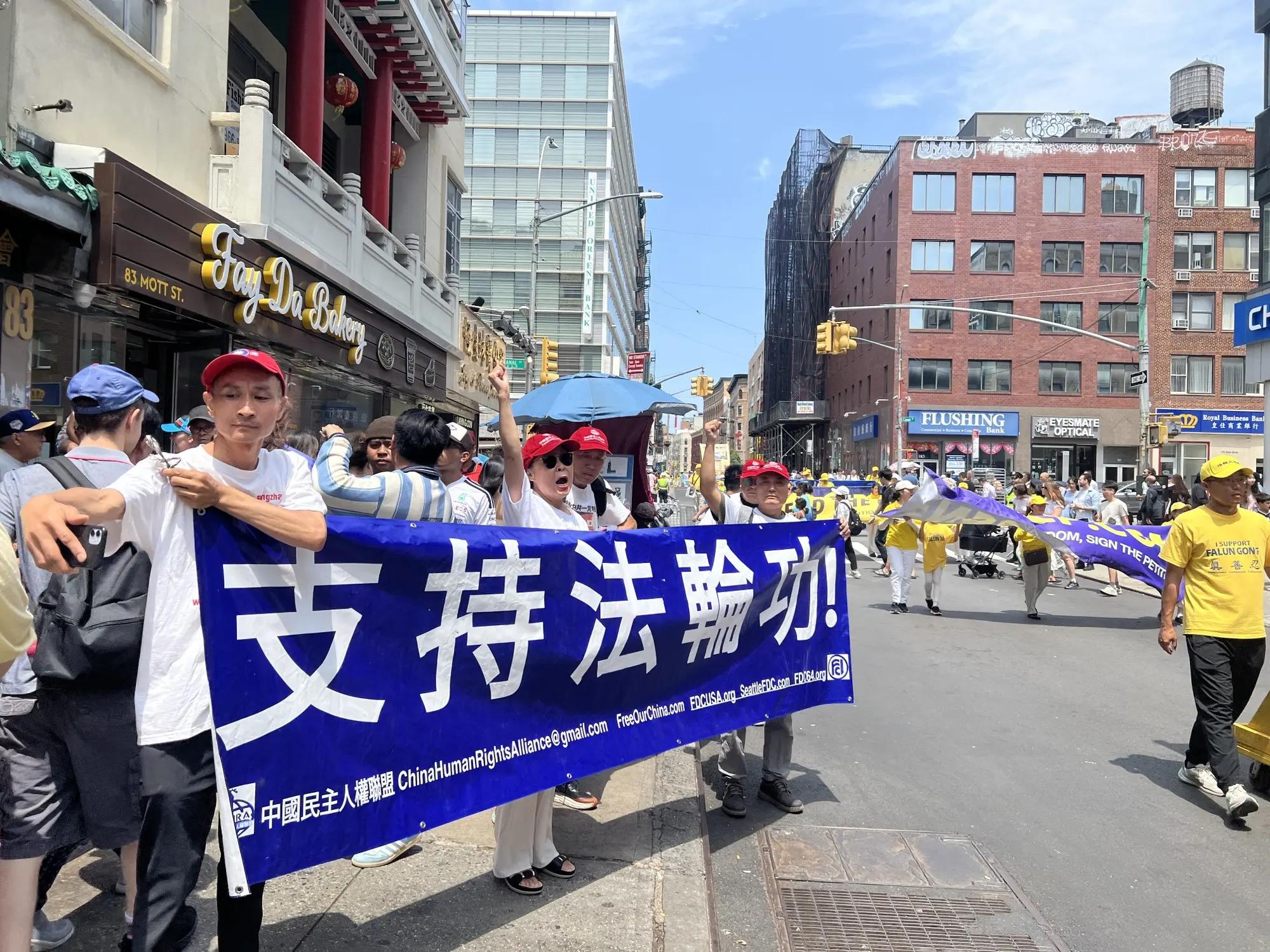 7月19日,紐約法輪功學員遊行的路上,有多位華人民眾自發地打出橫幅前來聲援法輪功學員。趙女士(中間喊口號)受訪時表示中共就是撒旦。(施萍/大紀元)